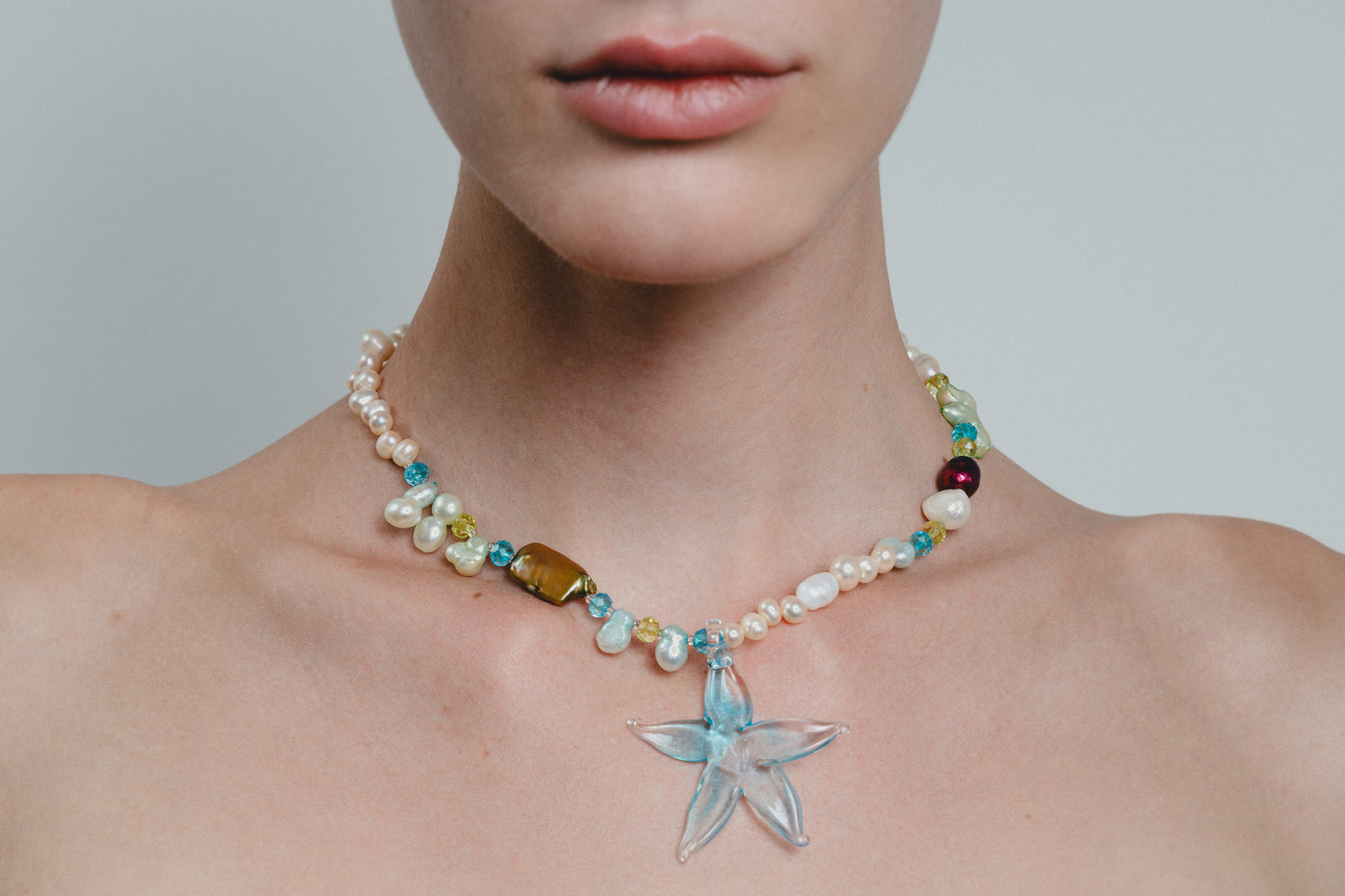 Necklace with starfish pendant worn by a person on a plain background