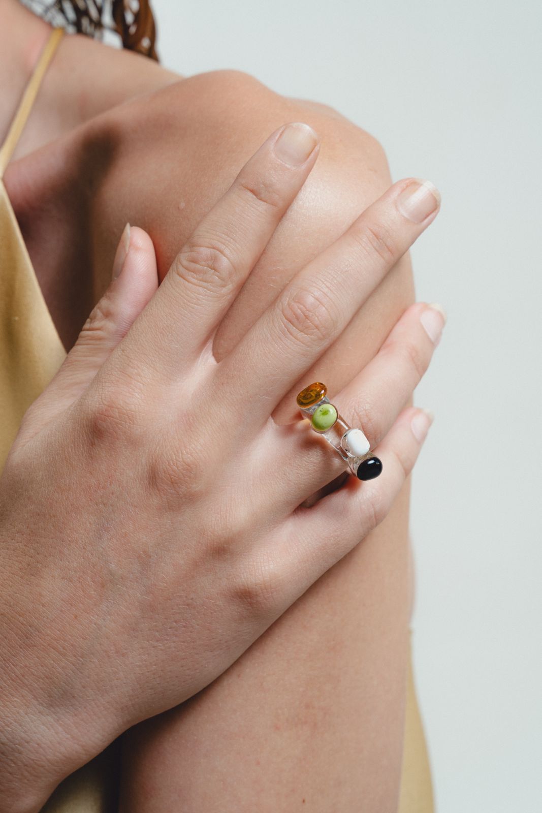 Close-up of a hand wearing a ring with colorful beads on a neutral background