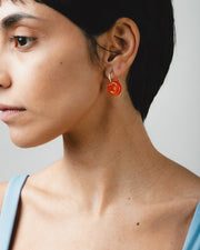 A pair of orange earrings in the shape of a donut, on a golden hoop, made from recycled glass