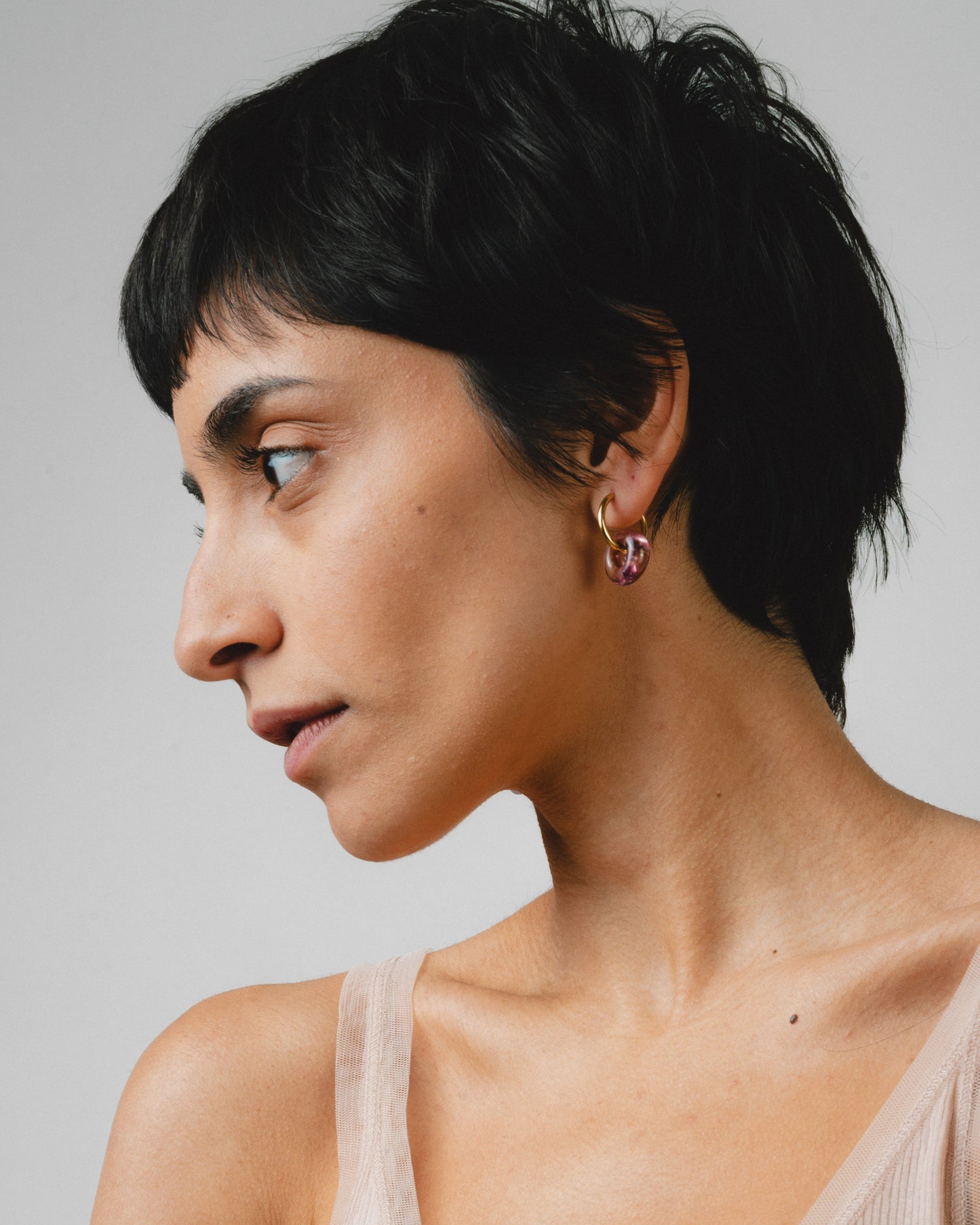 A model wearing purple hoop earrings on a base of golden stainless steel, made from recycled glass