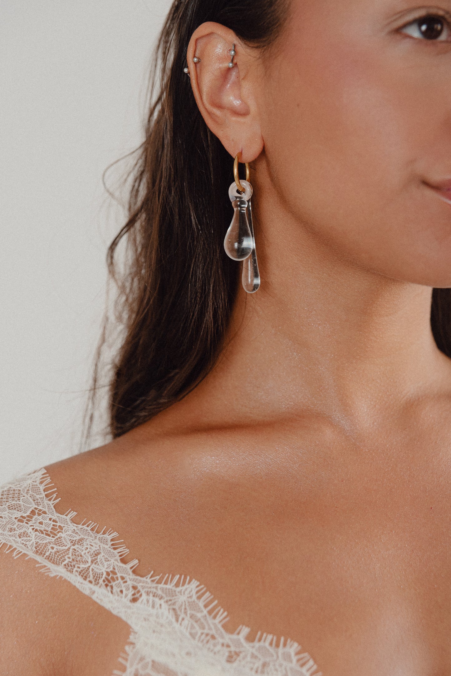 A clear, transparent drop-shaped earring on a gold hoop, made from recycled glass