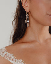 A clear, transparent drop-shaped earring on a gold hoop, made from recycled glass