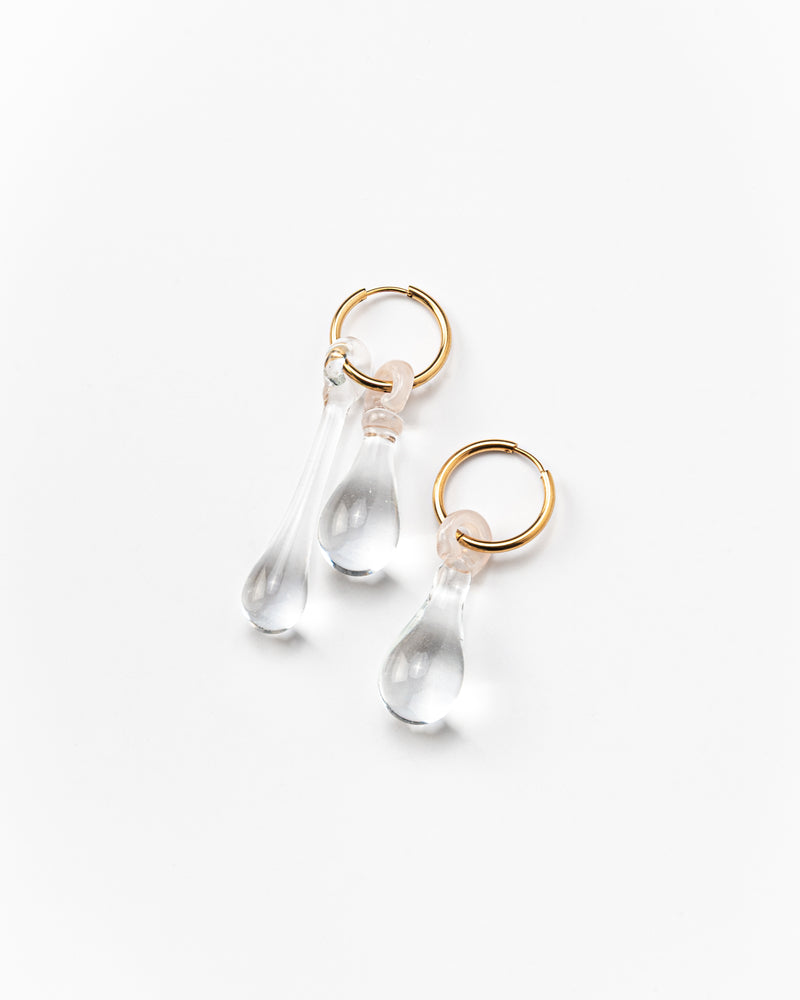 Pair of assymetrical clear, transparent drop-shaped earrings on a golden hoop. made from recycled glass
