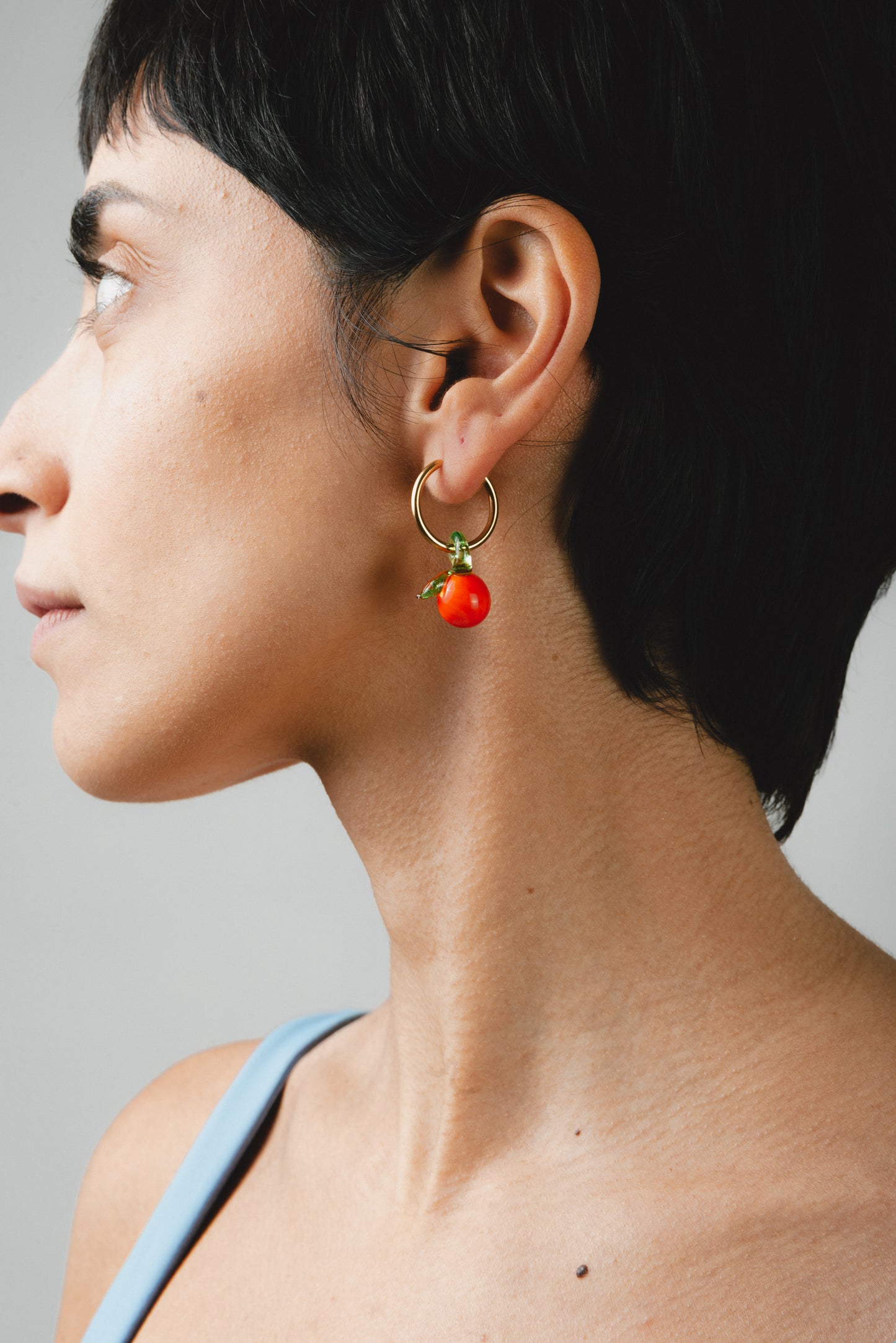 Gold hoop earrings featuring handcrafted orange-shaped charms made from recycled glass, detailed with delicate green leaves.
