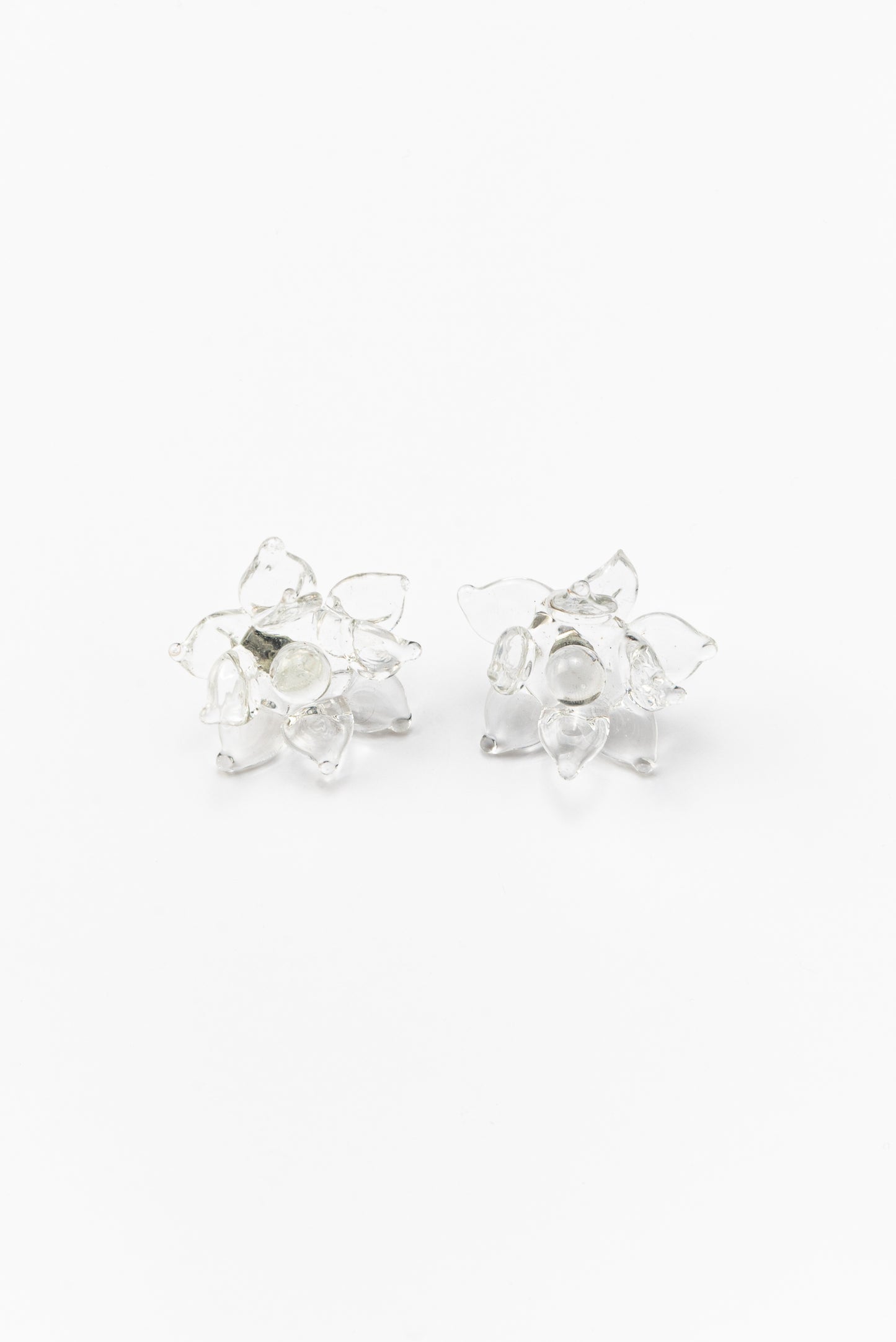 A pair of clear Pavonia stud earrings in a shape of a flower with spiky petals, made from recycled glass