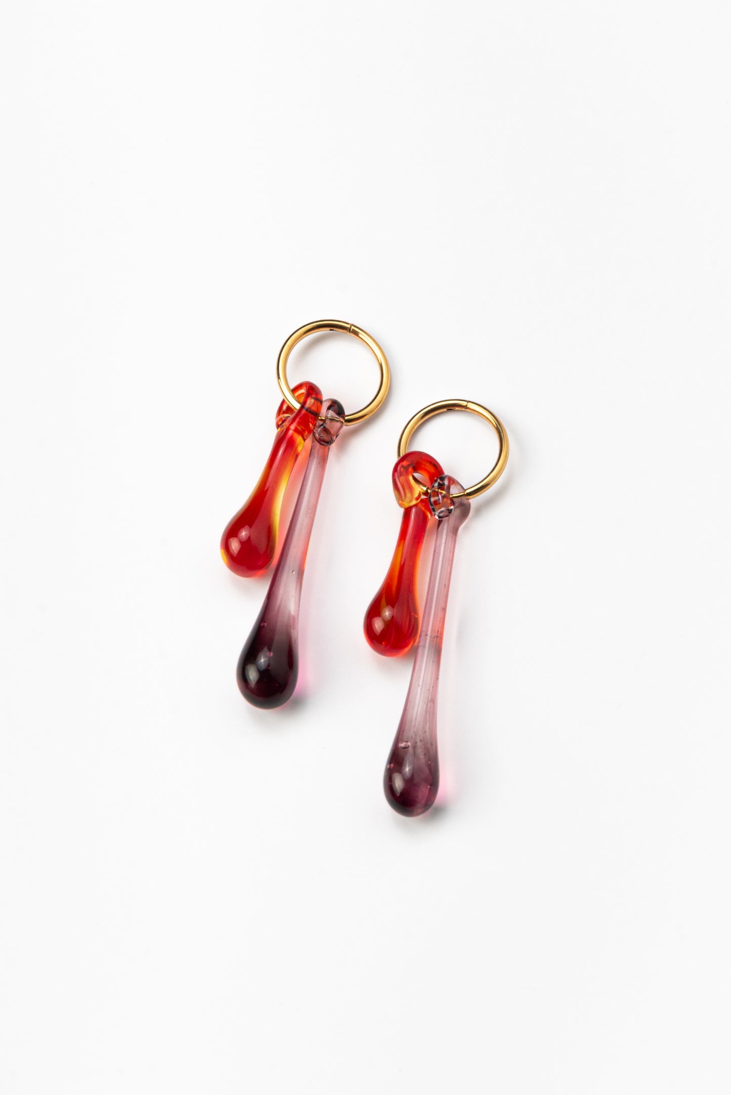 Gold hoop earrings with long red and purple gradient teardrop pendants made from recycled glass