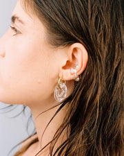A pair of clear, transparent oval earrings on a golden hoop, made from recycled glass