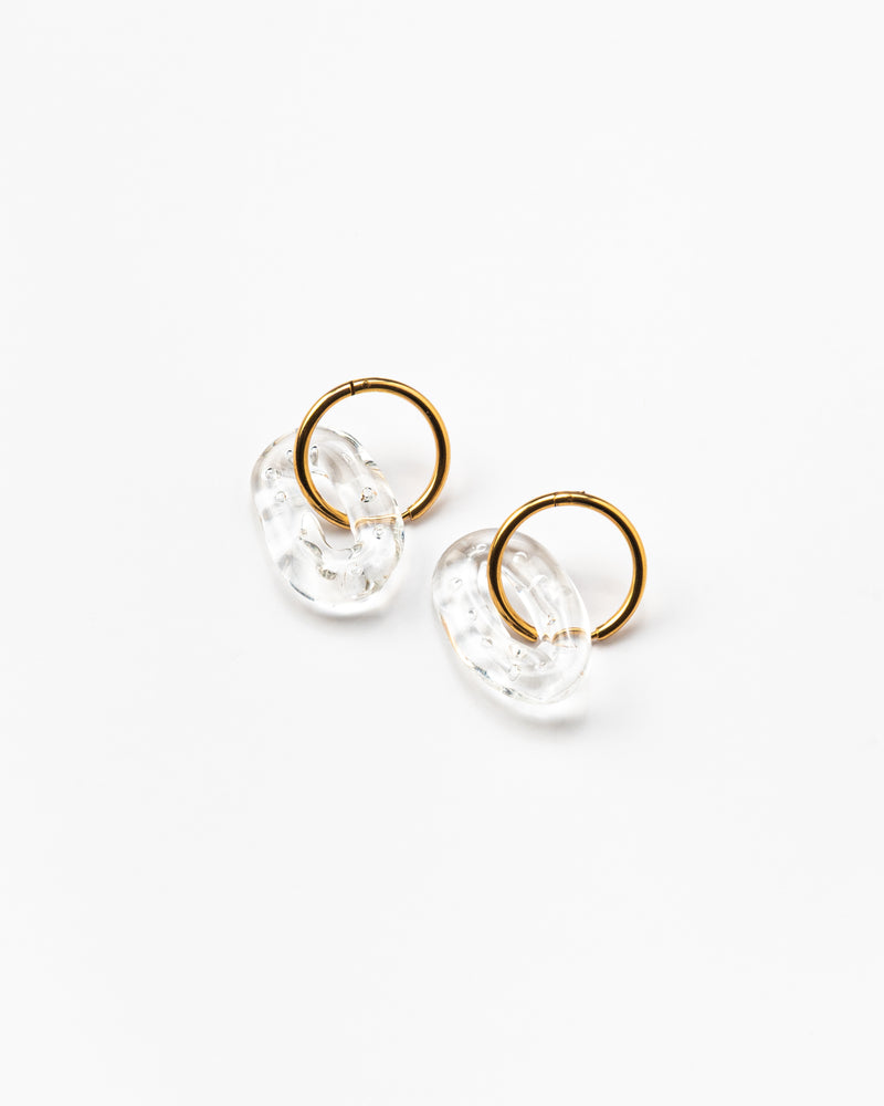 A pair of clear, transparent oval earrings on a golden hoop, made from recycled glass