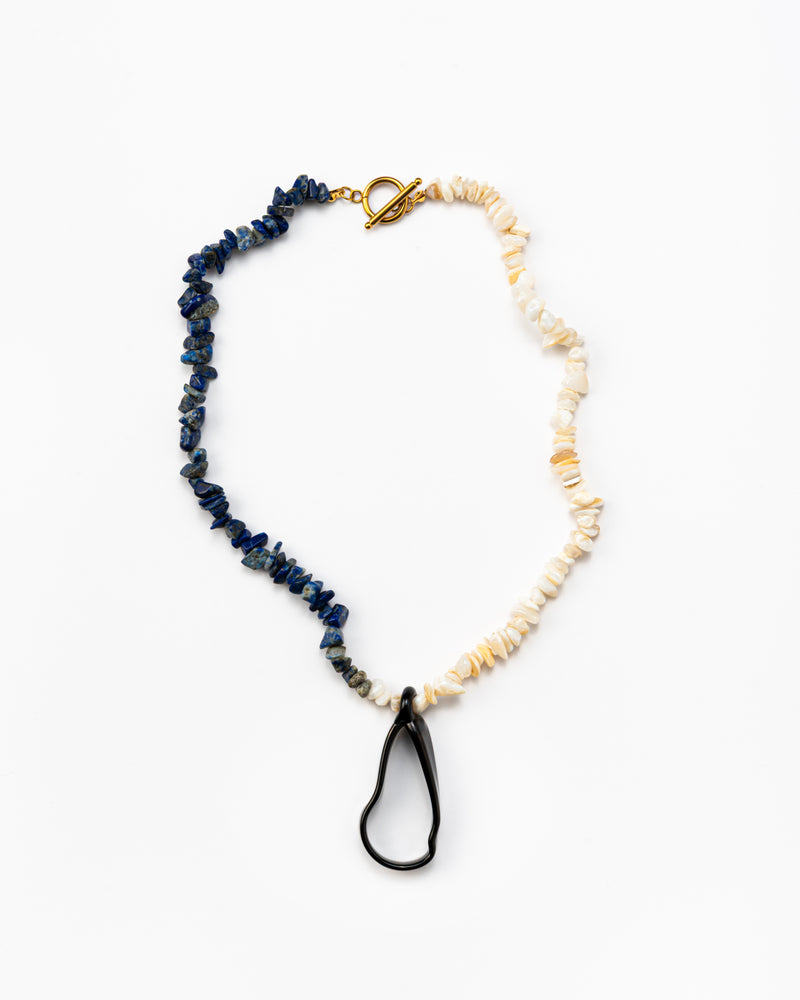 Necklace with half dark blue stone beads, half light beige stone beads, and a black teardrop pendant, with a gold toggle clasp, made from recycled glass