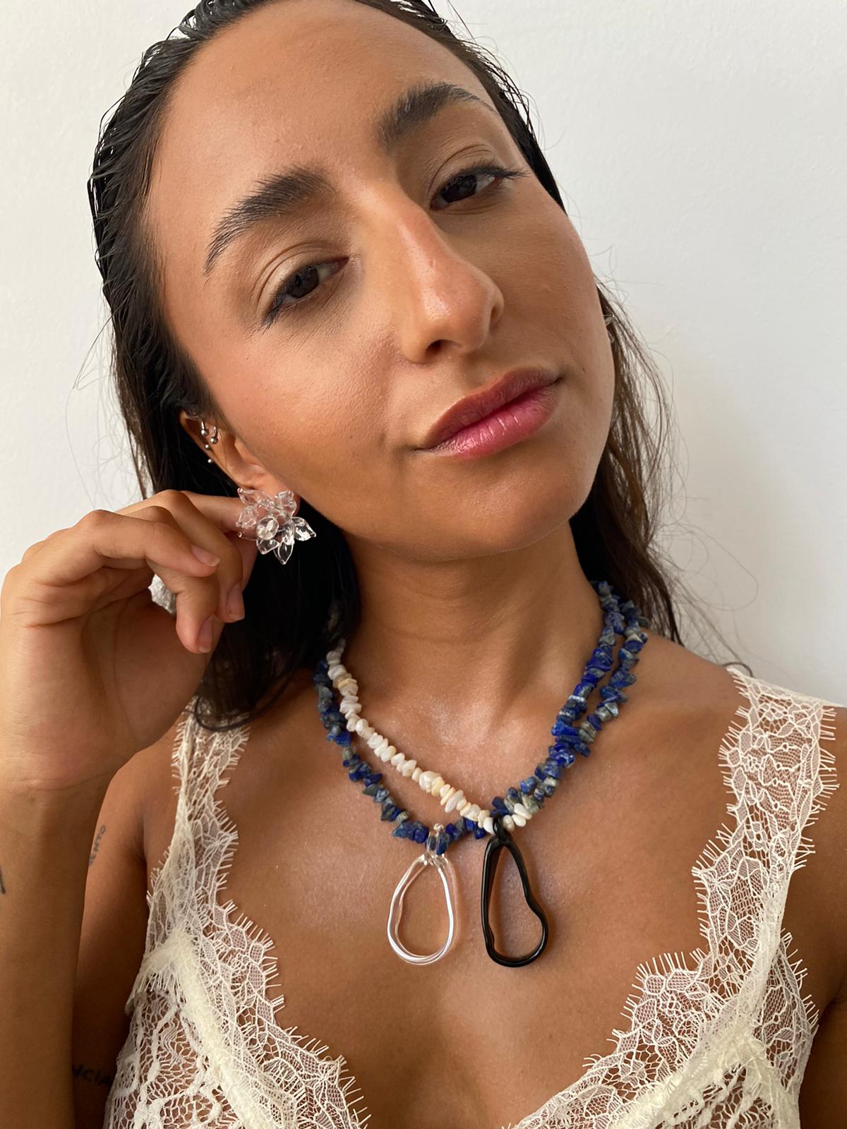 Two Menorca necklaces: First one with half dark blue stone beads, half light beige stone beads, and a black teardrop pendant made from recycled glass. Second one with deep blue gemstone beads and a clear teardrop pendant made from recycled glass.