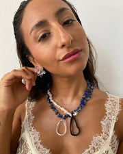 Two Menorca necklaces: First one with half dark blue stone beads, half light beige stone beads, and a black teardrop pendant made from recycled glass. Second one with deep blue gemstone beads and a clear teardrop pendant made from recycled glass.