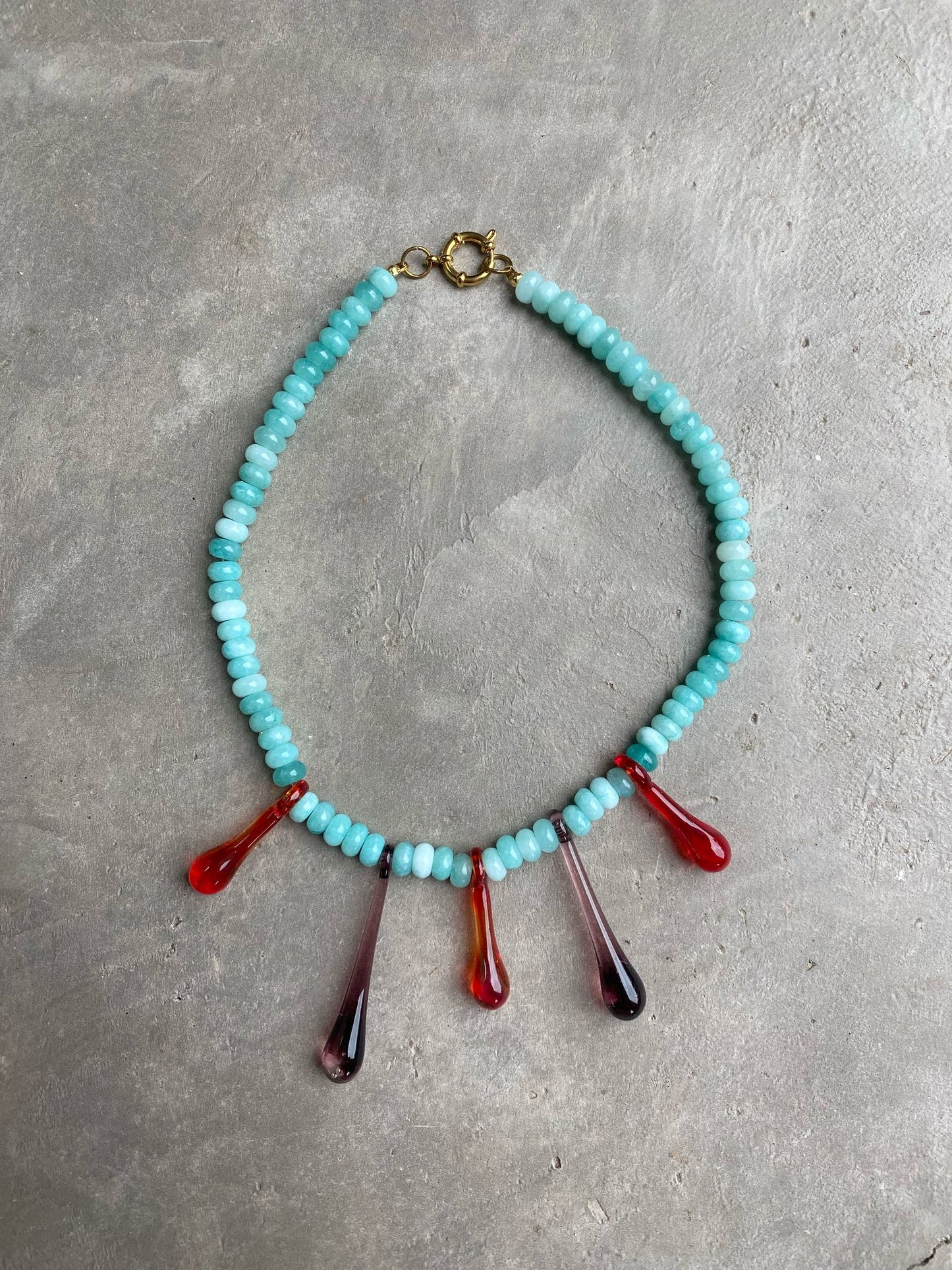 A statement necklace made of turquoise gemstone beads and red recycled glass drop pendants, with a gold toggle clasp