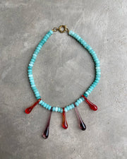 A statement necklace made of turquoise gemstone beads and red recycled glass drop pendants, with a gold toggle clasp