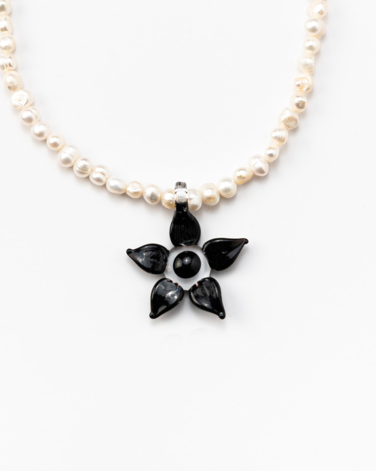 Necklace made of small white river pearls, featuring a gold toggle clasp and a large black flower pendant made from recycled glass
