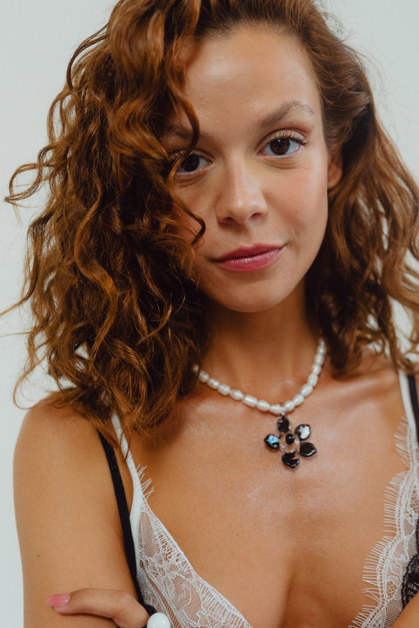 Necklace made of small white river pearls, featuring a gold toggle clasp and a large black flower pendant made from recycled glass