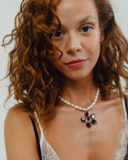 Necklace made of small white river pearls, featuring a gold toggle clasp and a large black flower pendant made from recycled glass