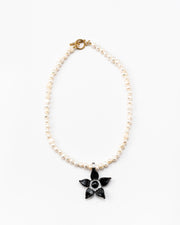 Necklace made of small white river pearls, featuring a gold toggle clasp and a large black flower pendant made from recycled glass