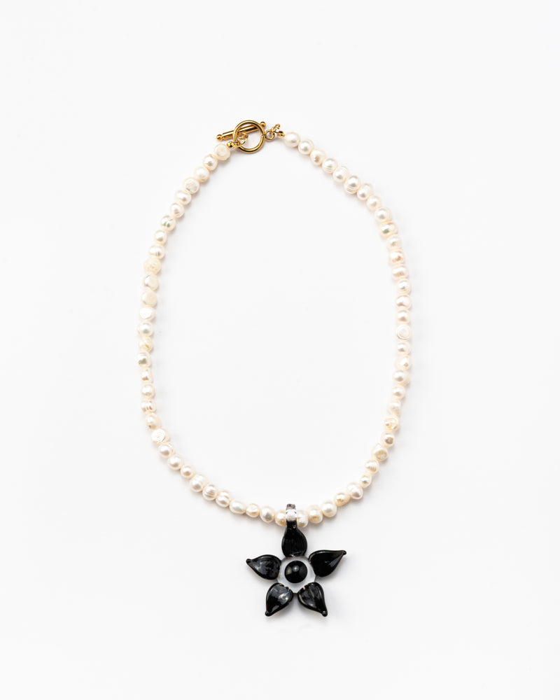 Necklace made of small white river pearls, featuring a gold toggle clasp and a large black flower pendant made from recycled glass