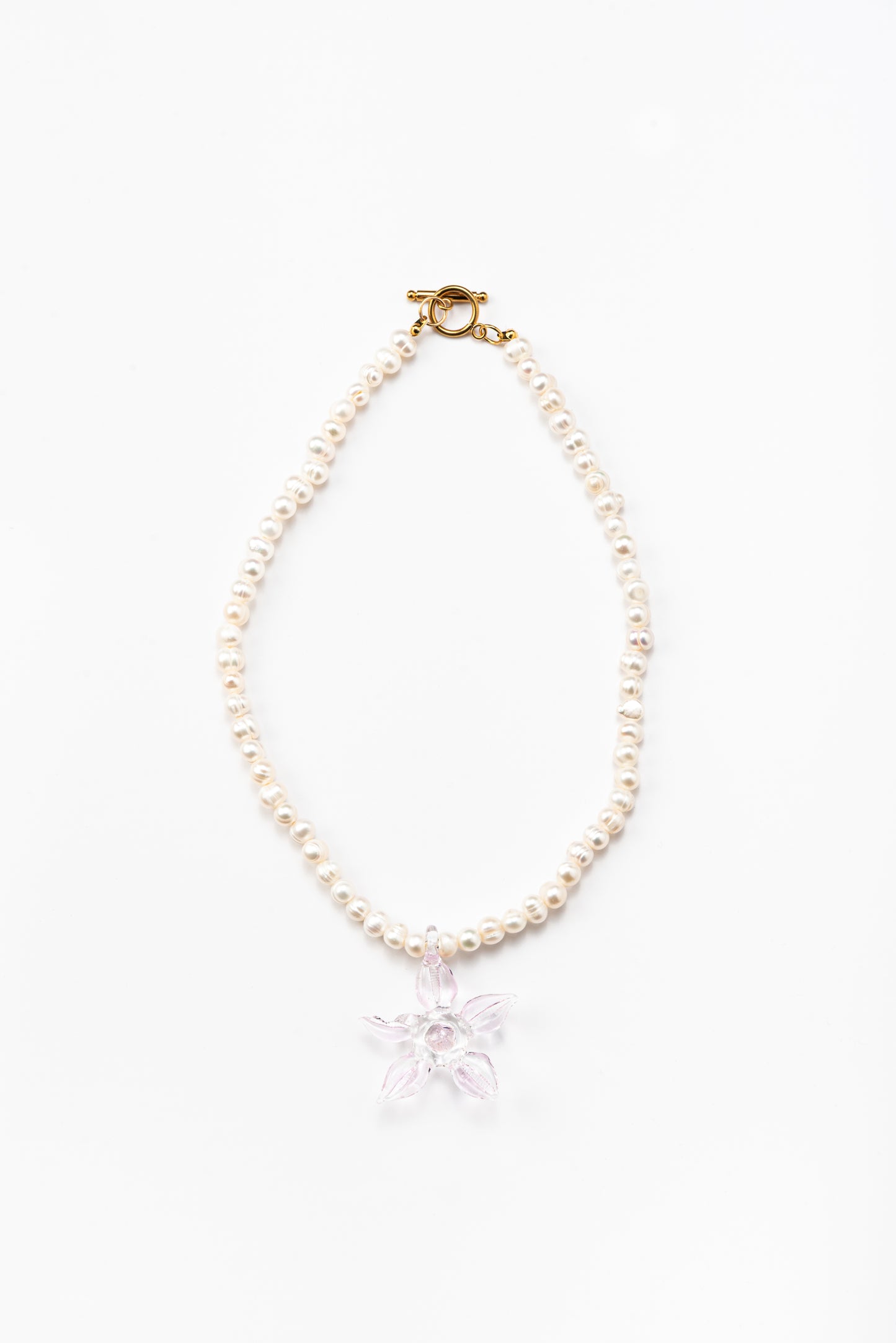 Necklace made of small white river pearls, featuring a gold toggle clasp and a large light pink flower pendant made from recycled glass