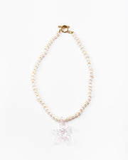 Necklace made of small white river pearls, featuring a gold toggle clasp and a large light pink flower pendant made from recycled glass
