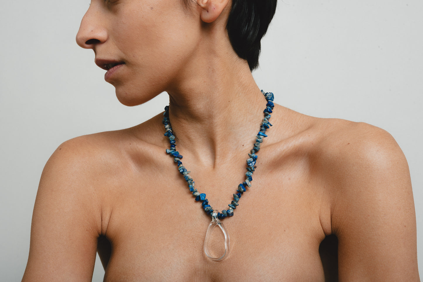 Necklace made of deep blue sea shell beads with a loop-shaped clear recycled glass pendant and a gold toggle clasp