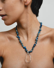 Necklace made of deep blue sea shell beads with a loop-shaped clear recycled glass pendant and a gold toggle clasp