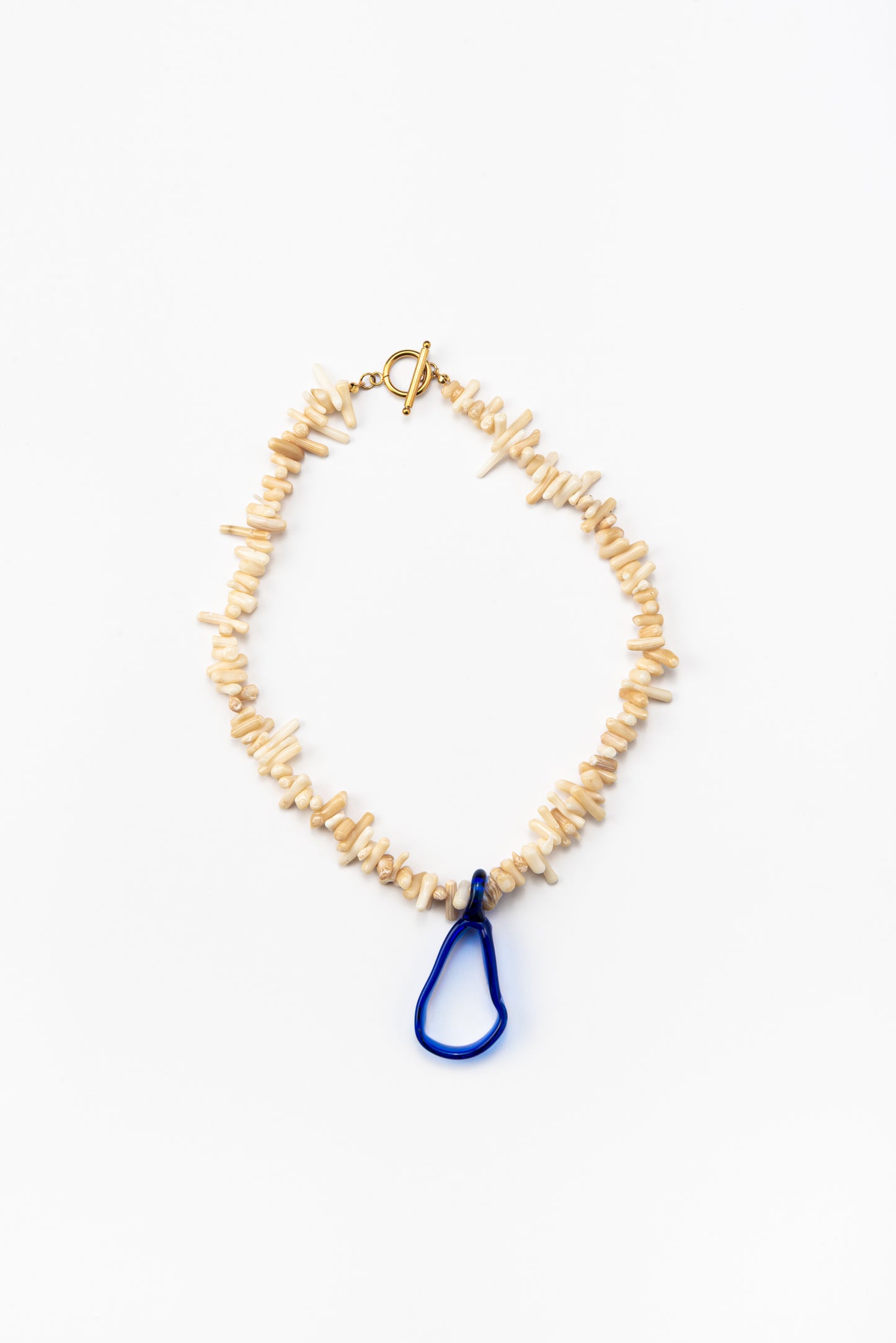 A necklace made of beige sea shell beads with a loop-shaped blue recycled glass pendant and a gold toggle clasp