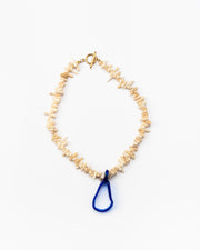 A necklace made of beige sea shell beads with a loop-shaped blue recycled glass pendant and a gold toggle clasp