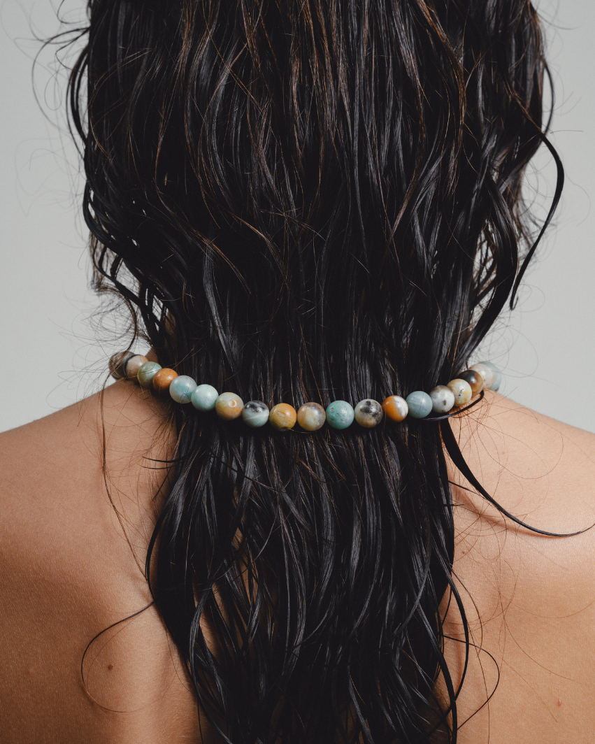 Person with a beaded hair tie in their wet hair against a neutral background