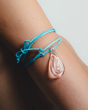 Turquoise bracelet with a pink teardrop charm on a wrist against a neutral background