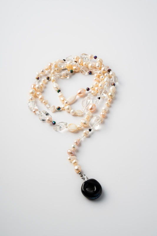 Pearl necklace with a black pendant on a light gray background

