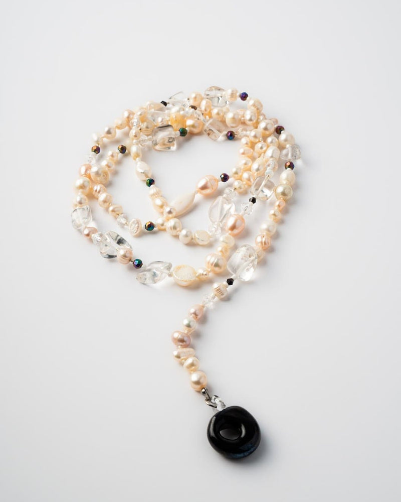 Pearl necklace with a black pendant on a light gray background

