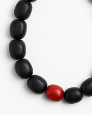 Black beaded necklace with a red accent bead on a white background