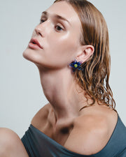 Woman wearing a blue top and floral earrings against a light gray background