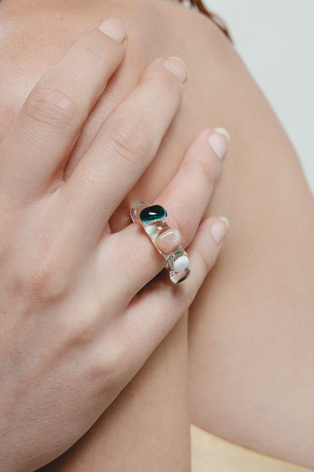 Close-up of a hand wearing a ring with a green gemstone on a neutral background