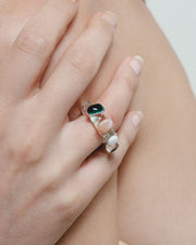 Close-up of a hand wearing a ring with a green gemstone on a neutral background