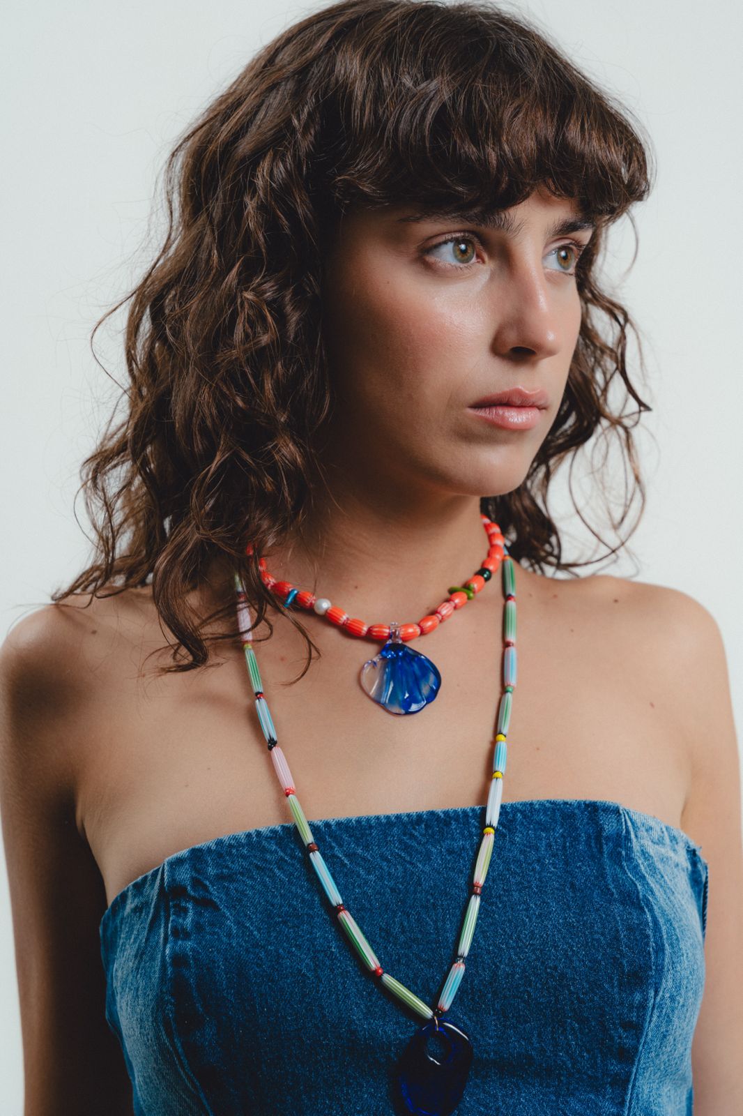 Woman wearing a colorful beaded necklace with a blue pendant against a white background