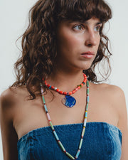 Woman wearing a colorful beaded necklace with a blue pendant against a white background