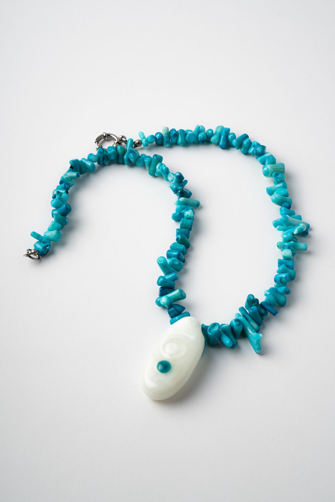 Turquoise beaded necklace with a white pendant on a light gray background