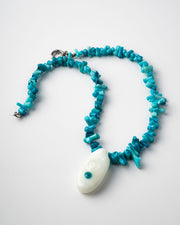 Turquoise beaded necklace with a white pendant on a light gray background