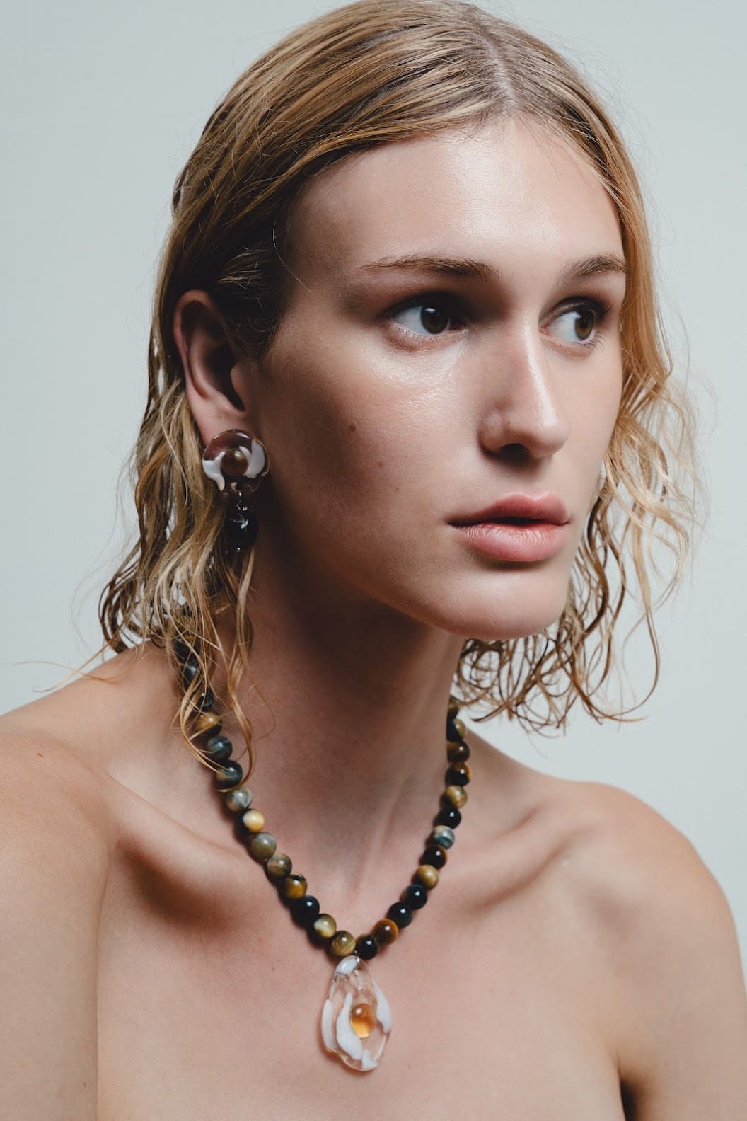 Woman wearing a beaded necklace with a pendant against a neutral background