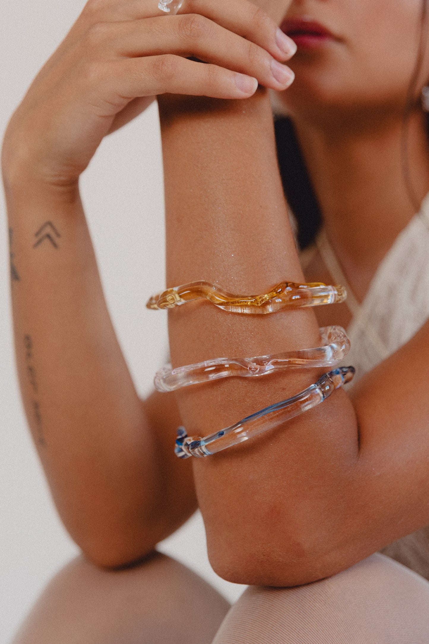 Wavy-shaped bracelets made of clear recycled glass with subtle pink, yellow, and blue accents