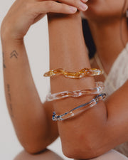 Wavy-shaped bracelets made of clear recycled glass with subtle pink, yellow, and blue accents