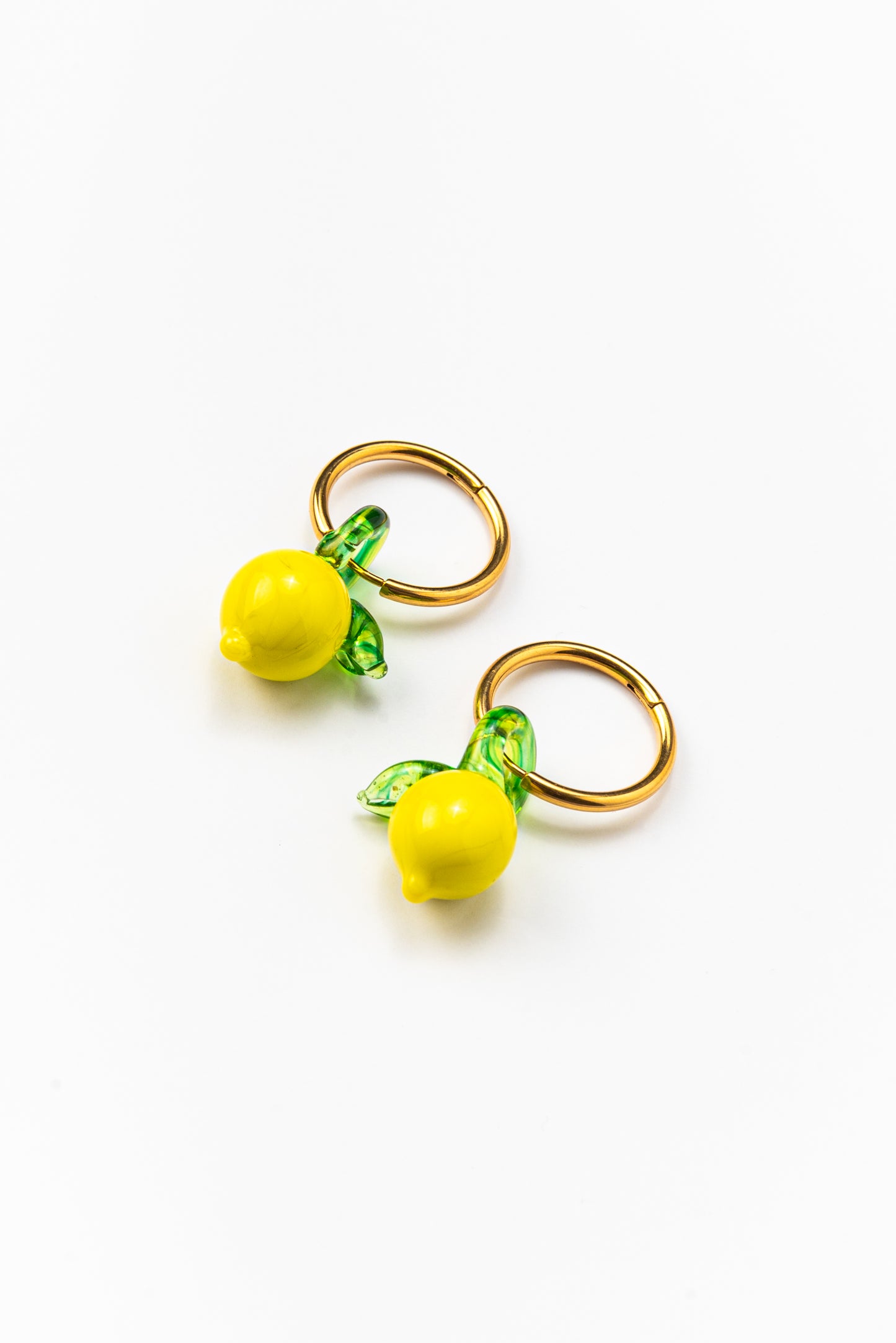 Gold hoop earrings featuring small yellow lemon-shaped pendants with green leaves, made from recycled glass