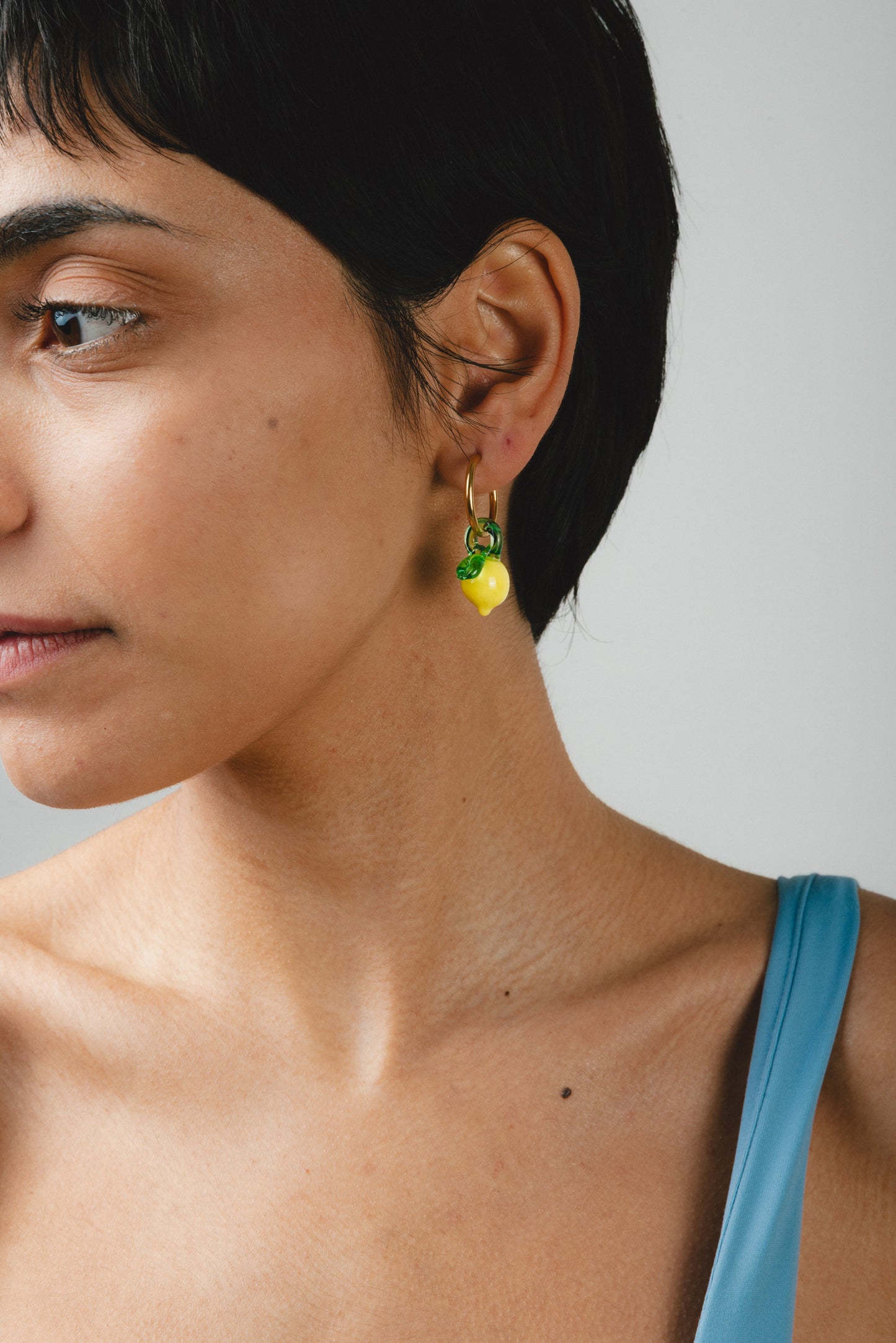 Gold hoop earrings featuring small yellow lemon-shaped pendants with green leaves, made from recycled glass