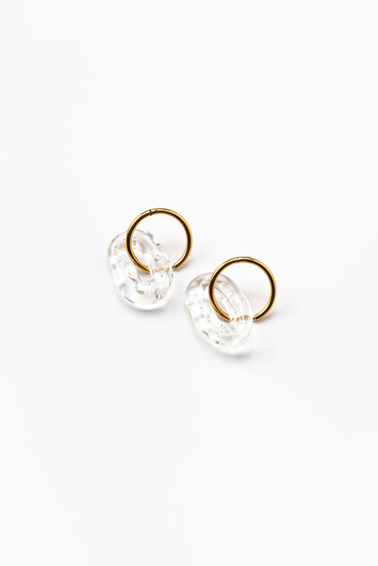 A pair of clear, transparent oval earrings on a golden hoop, made from recycled glass