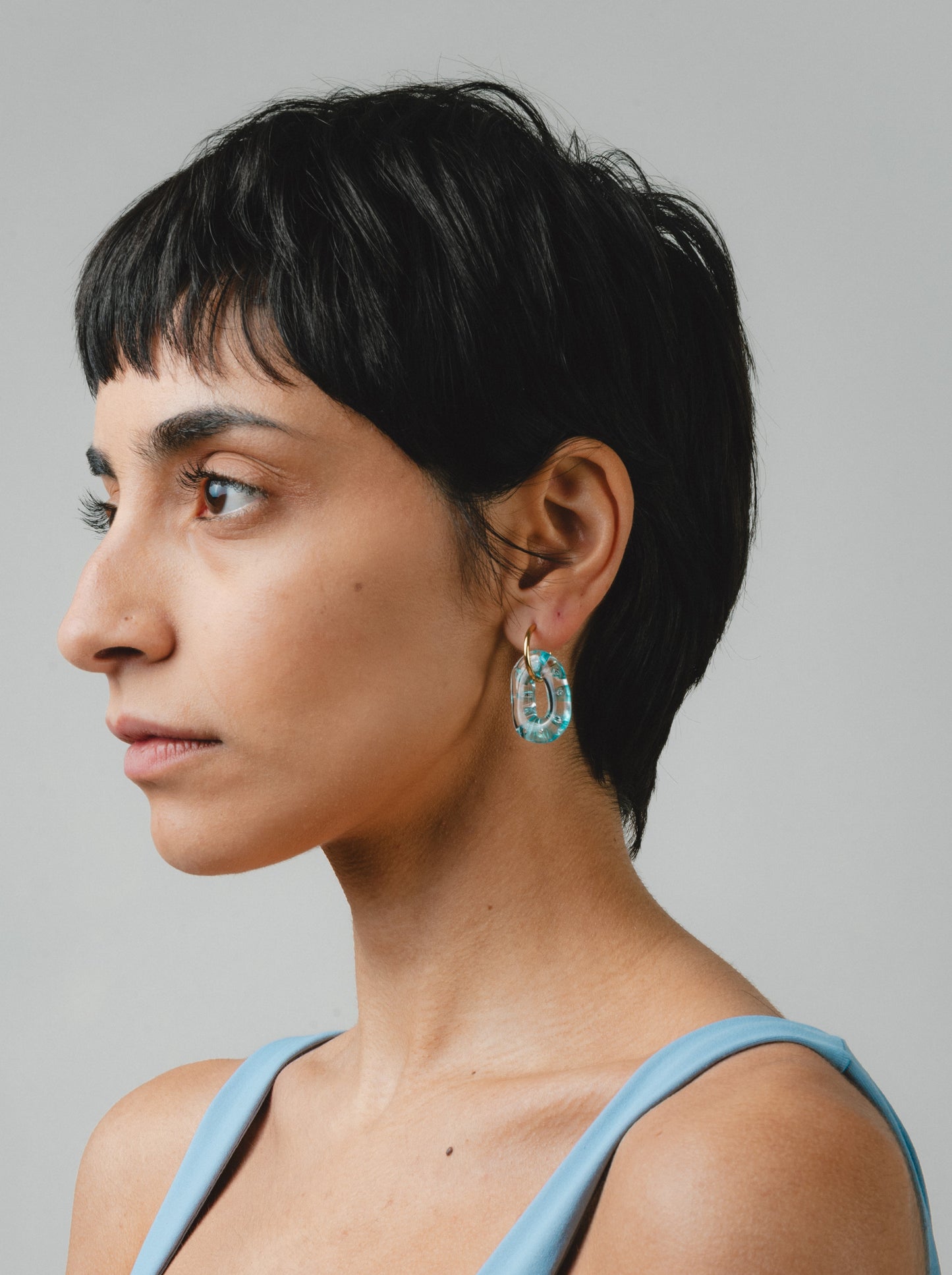 Clear oval earrings with little turquoise spheres inside, on a golden hoop, made from recycled glass