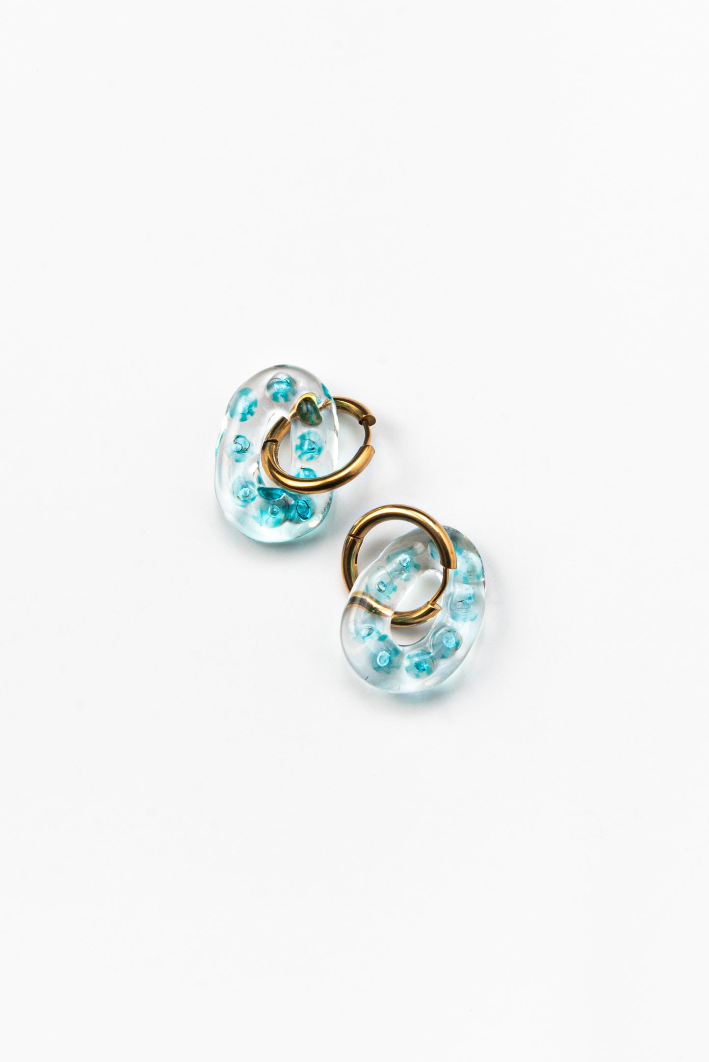 Clear oval earrings with little turquoise spheres inside, on a golden hoop, made from recycled glass