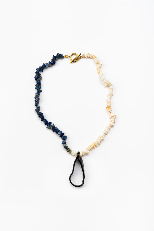 Necklace with half dark blue stone beads, half light beige stone beads, and a black teardrop pendant, with a gold toggle clasp, made from recycled glass