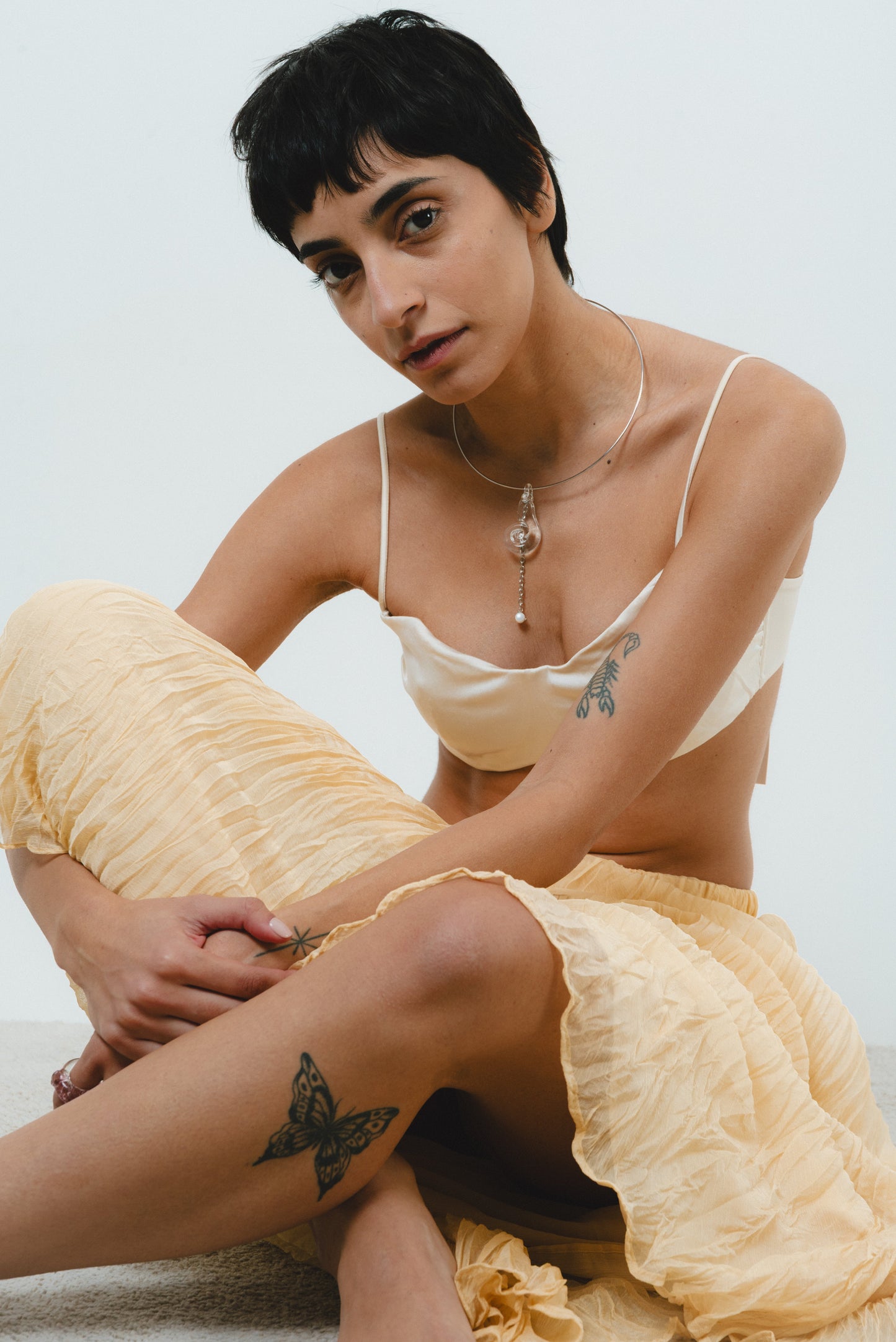 A silver necklace featuring a clear pendant in the form of a shell, made from recycled glass, and a drop chain with a white river pearl at the end